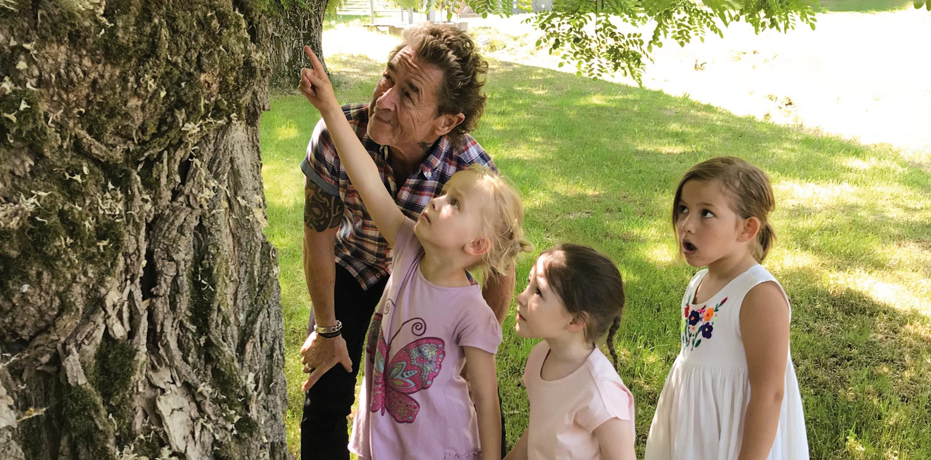 Peter Maffay mit drei Mädchen, die an einem Baum etwas entdeckt haben.