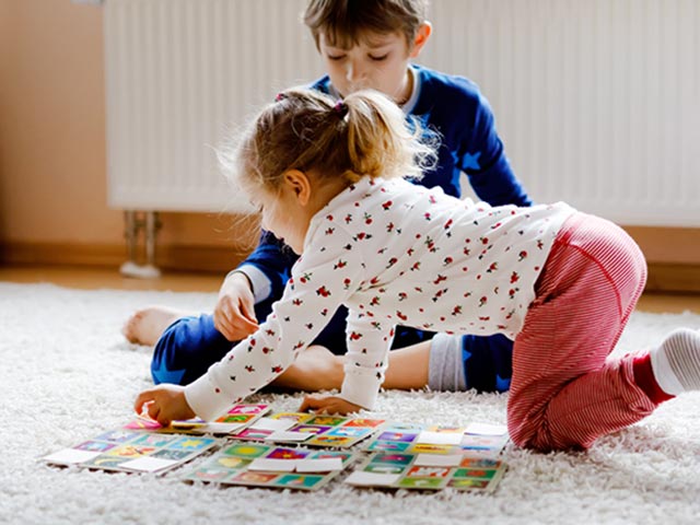 Junge und Mädchen spielen auf einem Teppichboden Memory