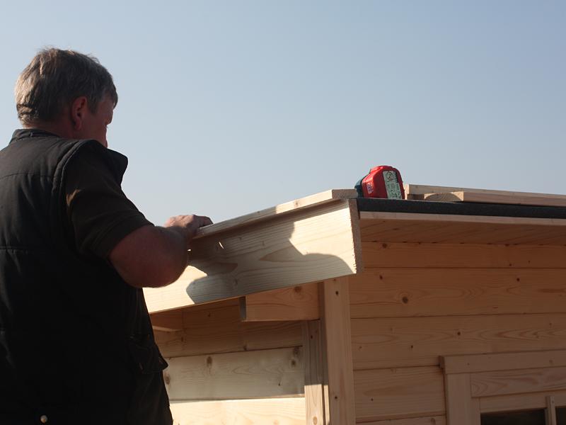 Monteur befestigt Dachblende an einem Gartenhaus