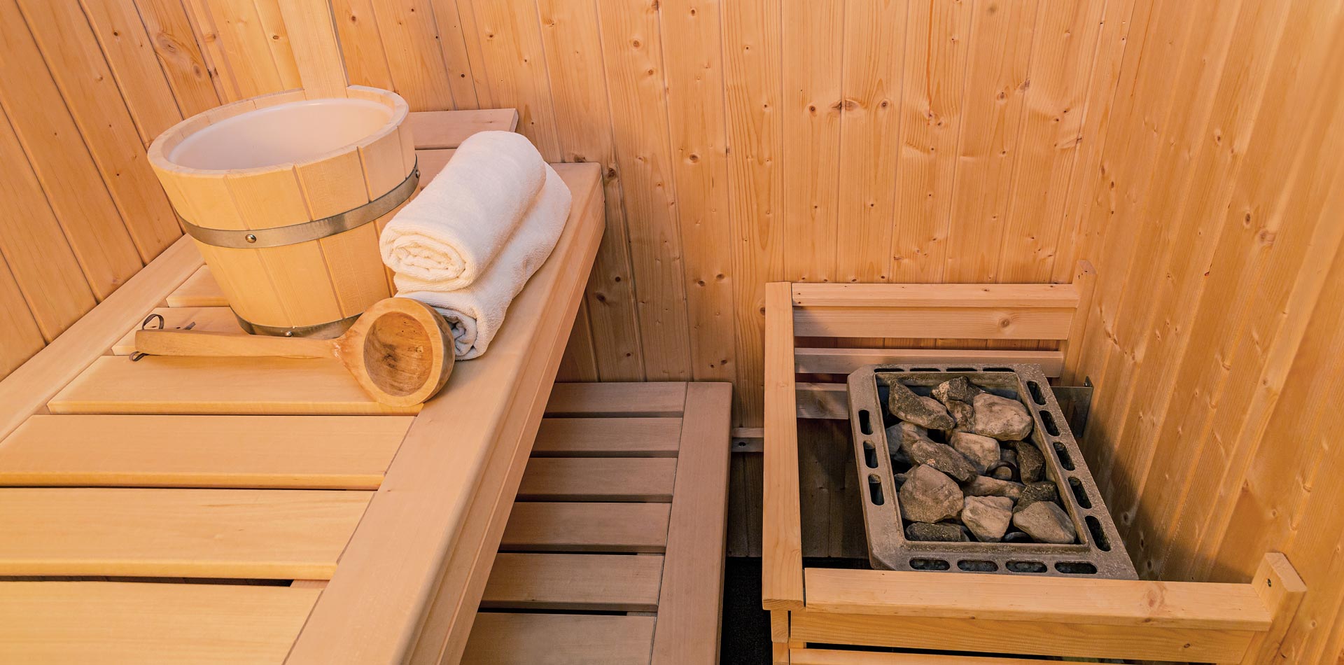 Saunaofen, Schöpfkelle, Aufgusskübel und Handtücher in einer Holzsauna