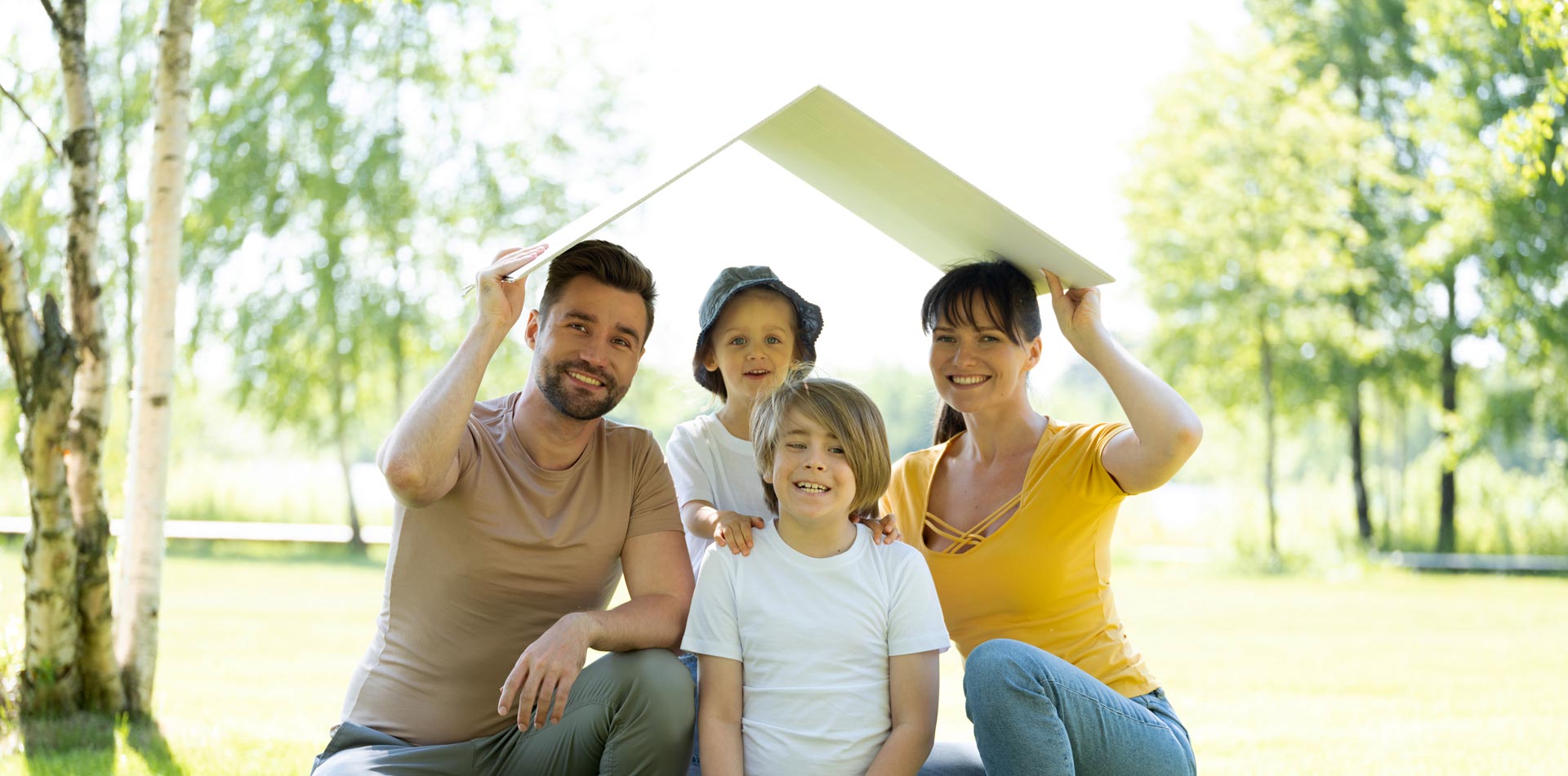 Glückliche Familie mit Satteldach aus Pappe auf Ihrem neuen Grundstück.