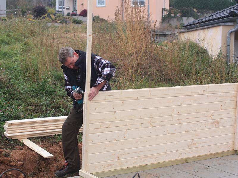 Mann verschraubt Wandbohlen beim Aufbau eines Gartenhauses